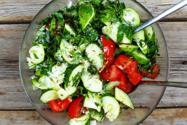 Ahşap bir masa üzerinde şeffaf bir kasede bahar detoks salata. Yukarıdan görüntüleyin. Salata taze salatalık ve domates, otlar ve tohum ile