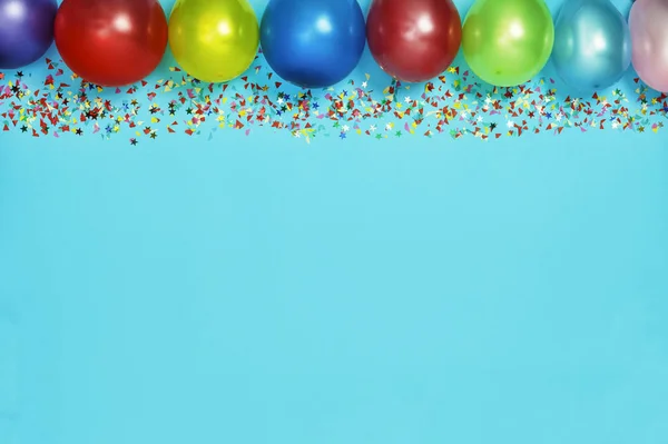 Multicolor party or birthday background on blue with a frame of colorful party balloons, streamers, confetti and candy around central copy space