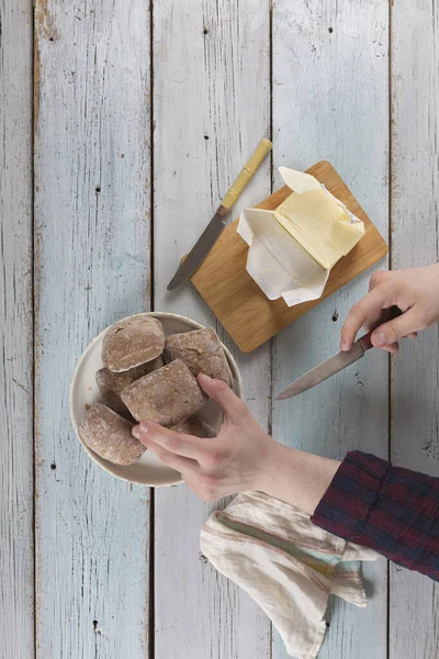 Young man buttering butter on bun, on an old rustic table. Banner