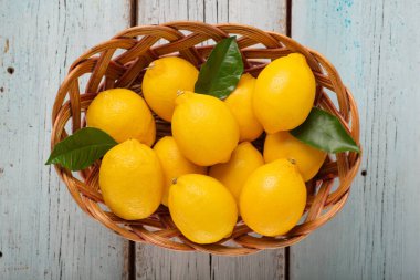 Mavi ahşap bir arka planda hasır sepette olgun limonlar.