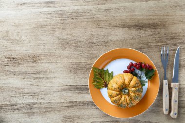 Autumn Thanksgiving composition on a rustic wooden table with orange pumpkin and viburnum branch with red berries and green leaves. Empty space for text