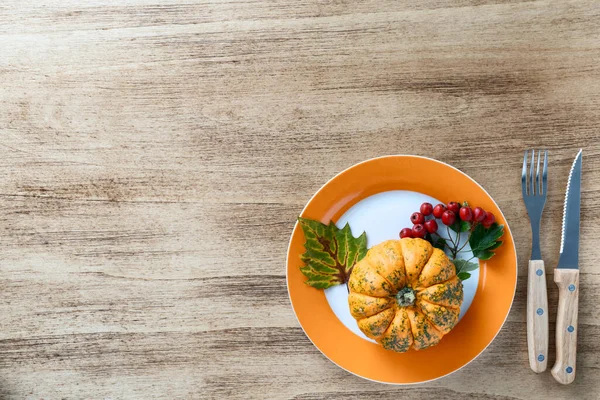 Autumn Thanksgiving composition on a rustic wooden table with orange pumpkin and viburnum branch with red berries and green leaves. Empty space for text