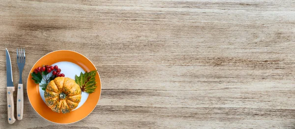 Autumn Thanksgiving composition on a rustic wooden table with orange pumpkin and viburnum branch with red berries and green leaves. Empty space for text