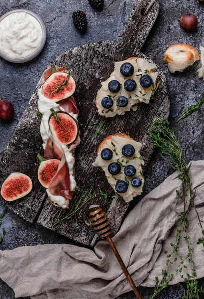 Taze Fransız baget ile krem peynir, incir, yaban mersini ve jambon eski ahşap tahta üzerinde gri beton arka plan üzerinde servis