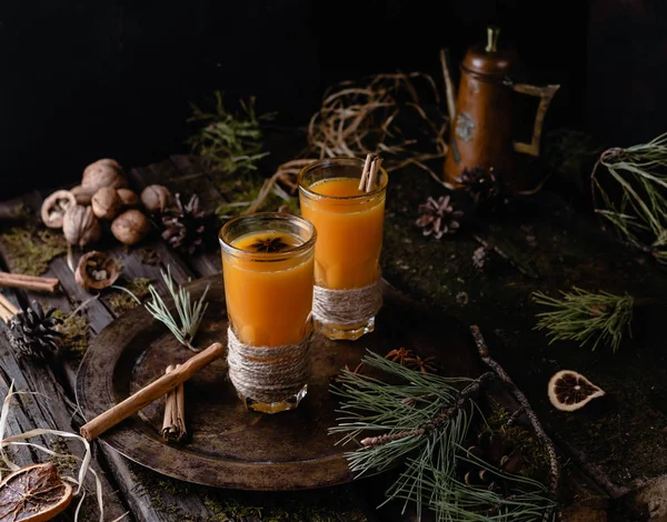 hot sea buckthorn drinks with spices in high glasses on vintage tray among pine branches with winter decor on old wooden table