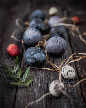 Koyu ahşap arka planda kırmızı çilek ile renkli bıldırcın yumurtaları yığını 