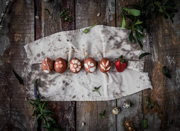 Row of easter eggs with natural ornaments on cotton towel over wooden background