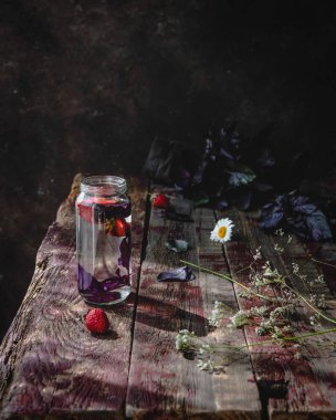 Eski ahşap masada çilek ve mor fesleğen ile su cam 