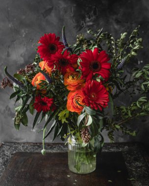 Kırmızı gerbera, ranunculuses ve koyu taş arka planda yeşillikler ile taze bahar buket