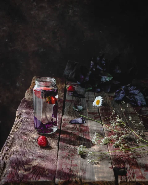 Eski ahşap masada çilek ve mor fesleğen ile su cam 