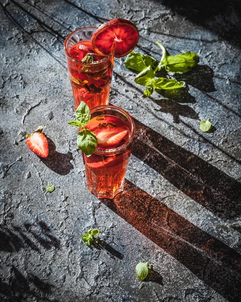 Strawberry lemonade with blood oranges in glasses on shabby grey concrete background
