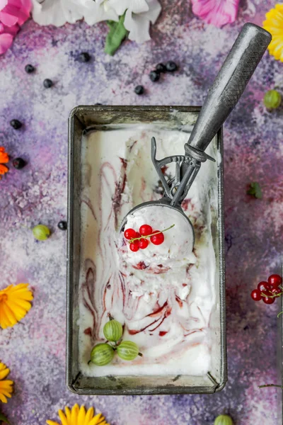 Berry ice cream in metal box on concrete background with flowers and berries