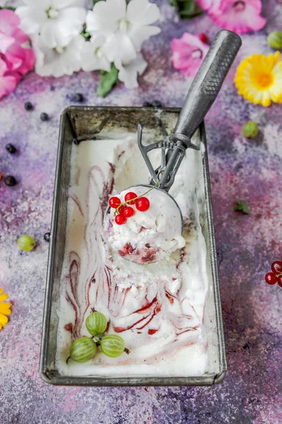 Berry ice cream in metal box on concrete background with flowers and berries