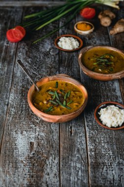Sıcak, lezzetli sebze çorbası, yeşil soğanlı kase, pirinç tabağı, ahşap masa, yakın görüş. 