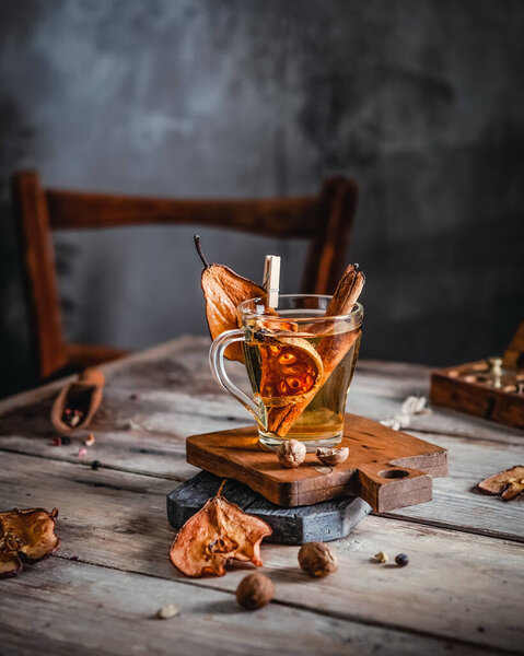 herbal tea with orange and pear with cinnamon stick in glass on wooden table, toned for vintage effect