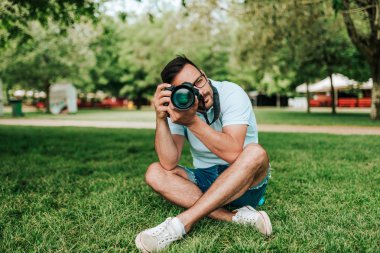 Parkta çim üzerinde oturan fotoğrafçı.