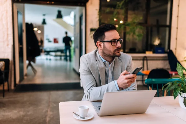 serious young businessman waiting for call holding smartphone