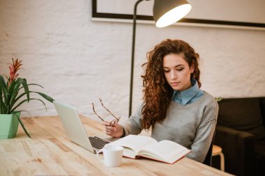 evde eğitim, kitap okuma ve dizüstü bilgisayar kullanarak çekici genç kadın