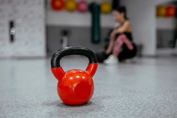red kettle bell and blurred woman sitting on the floor in background