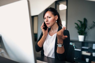 Kadın yönetici bilgisayar ekranına bakarak ve ciddi konuşmayı telefonda yapıyor.