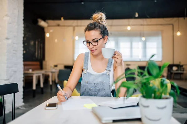 Kafede okuyan öğrenci kız. Kalemle yazma ve bir fincan holding.