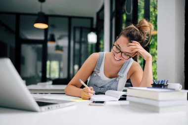 Ders kitapları notlar alarak gülümseyen genç kadın.