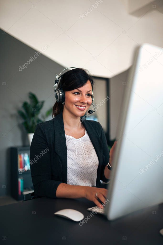 Portrait of beautiful businesswoman with headset working on computer.