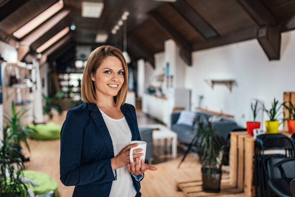 Portrait of female entrepreneur holding a mug in open space office.