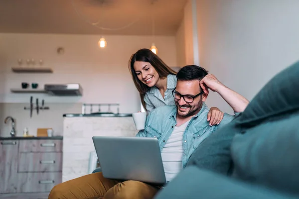 Two young people using laptop while sitting on the couch.