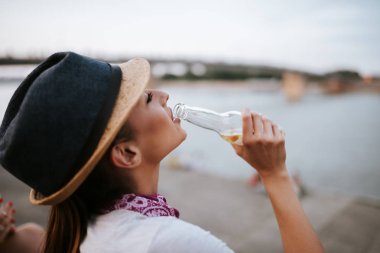 Güzel kız açık havada otururken bir şişeden içme yakın çekim görüntüsü.