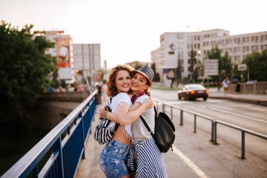 Yaz aylarında açık havada sarılma bir iki kız portresi. Kameraya bakarak.