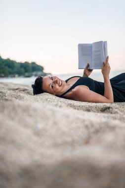 Bir kitap okuma sahilde, döşeme güzel bir kadın. Kopya alanı.