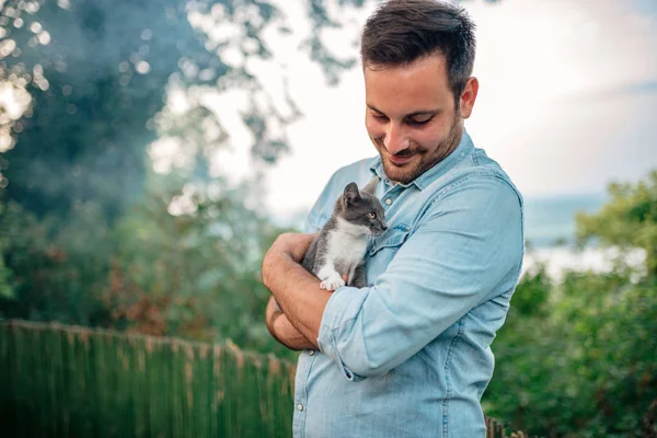 Handsome man hugging a cat outdoors.