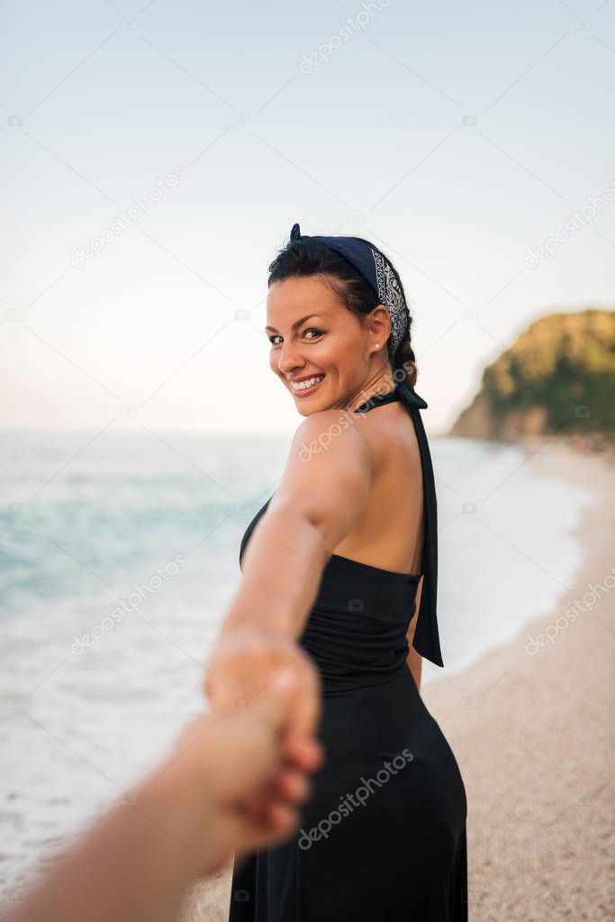 Smiling woman holding man's hand while walking on the beach.