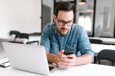 Modern ofis masasında otururken telefon kullanan genç adam.