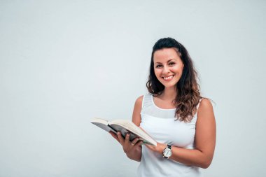 Güzel genç kadın izole arka plan üzerine bir kitap okuma. Kameraya bakıyor. Kopya alanı.