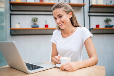 Laptop kapuçino yudumlarken gülümseyen kız.