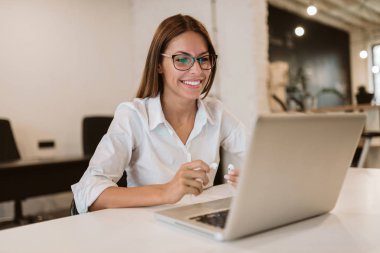 Office birlikte çalışma masasında gülümseyen genç iş kadını.