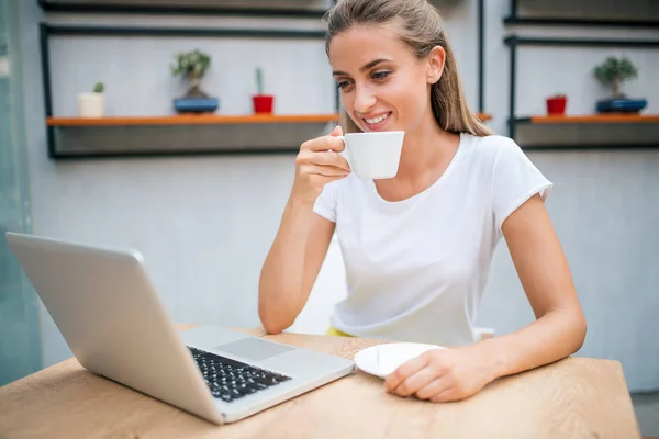 Lächelndes Mädchen Das Kaffee Trinkt Und Laptop Drinnen Benutzt — Stockfoto