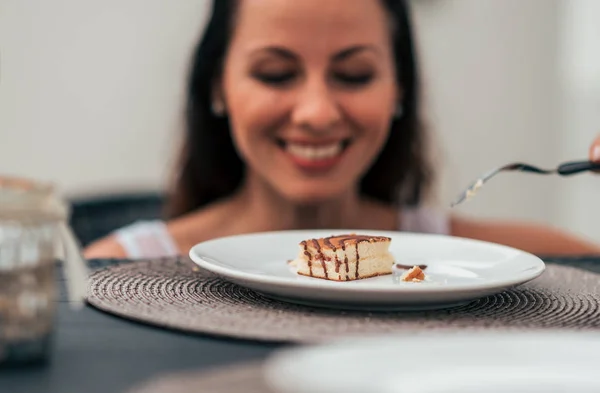 Young woman at the table ooking at cake. Focus on cake.