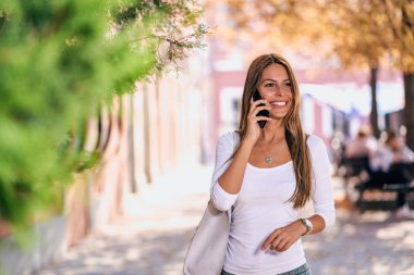 Sokakta yürürken cep telefonunuzla gülümseyen kadın.