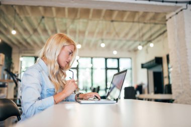 Parlak modern ofisinde çalışan genç kadın yan görünüm. Kopya alanı.