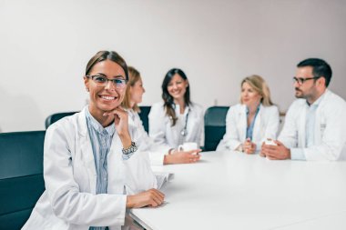 Güzel gülümseyen kadın doktor arkadaşları arka planda oturuyor iken kameraya bakıyor.