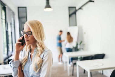 Telefonda konuşurken ciddi iş kadını. Arka plan beyaz tahta üzerinde çalışma arkadaşları.