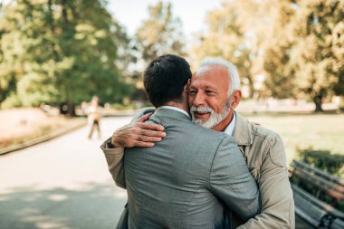 Yaşlı baba ve Yetişkin oğlu parkta sarılma.