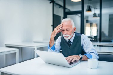 Modern ofis dizüstü bilgisayar ekranında bakarak endişeli üst düzey iş adamı.