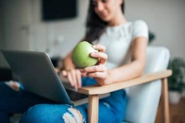 Yeşil elma laptop evde kullanırken tutan genç kadın. Elma ön odaklanmak.