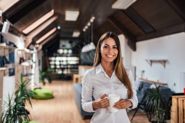 Bir kupa tutarak ve kamera modern çatı katında bakarak çekici genç bir kadın portresi.