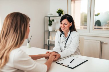 Gülümseyen kadın doktor kadın hastanın elini tutarak.