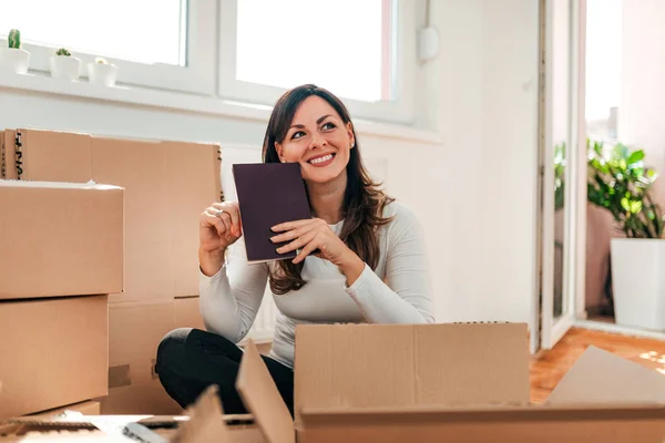 一个快乐的女人拿着一本书坐在盒子里的地板上的肖像 搬到新公寓 — 图库照片
